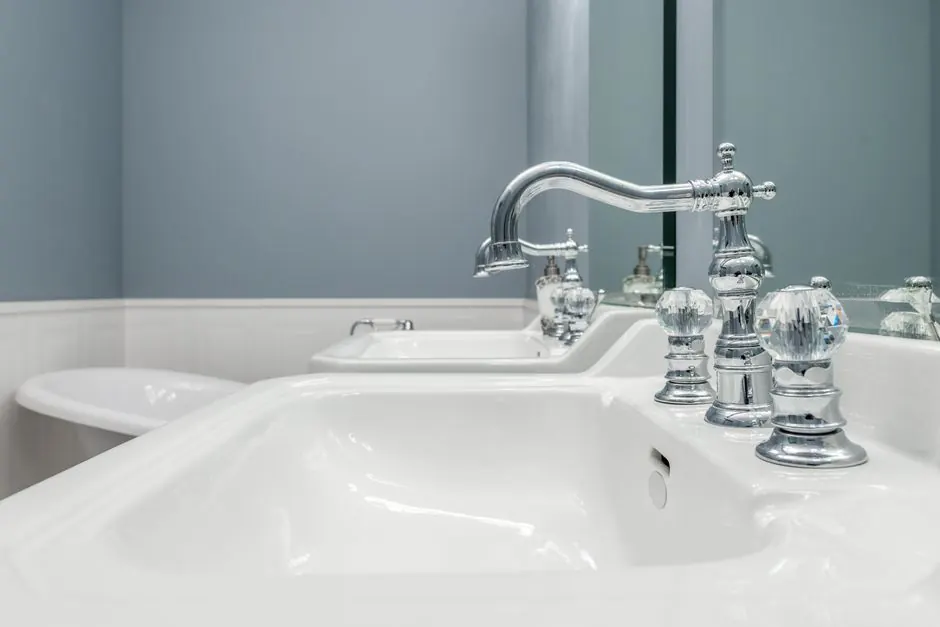 Clean white sinks with stylish metal faucets in light bathroom in luxury apartment